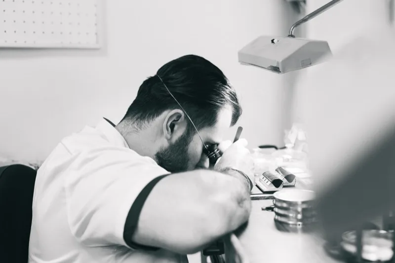 Artisan horloger au travail à la loupe sur son établi, photographie noir et blanc
