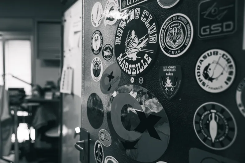 Porte de l'atelier ornée de stickers de clubs marseillais de plongée et d'aviron